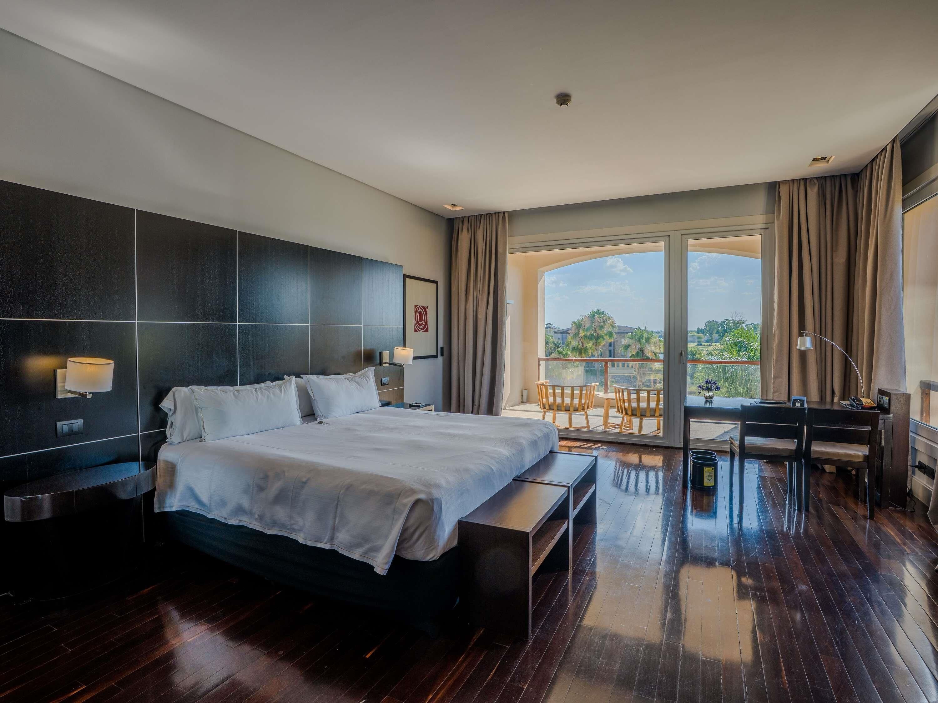 Ein modernes Hotelzimmer mit einem großen Bett, einem Schreibtisch und einem Balkon mit Blick.