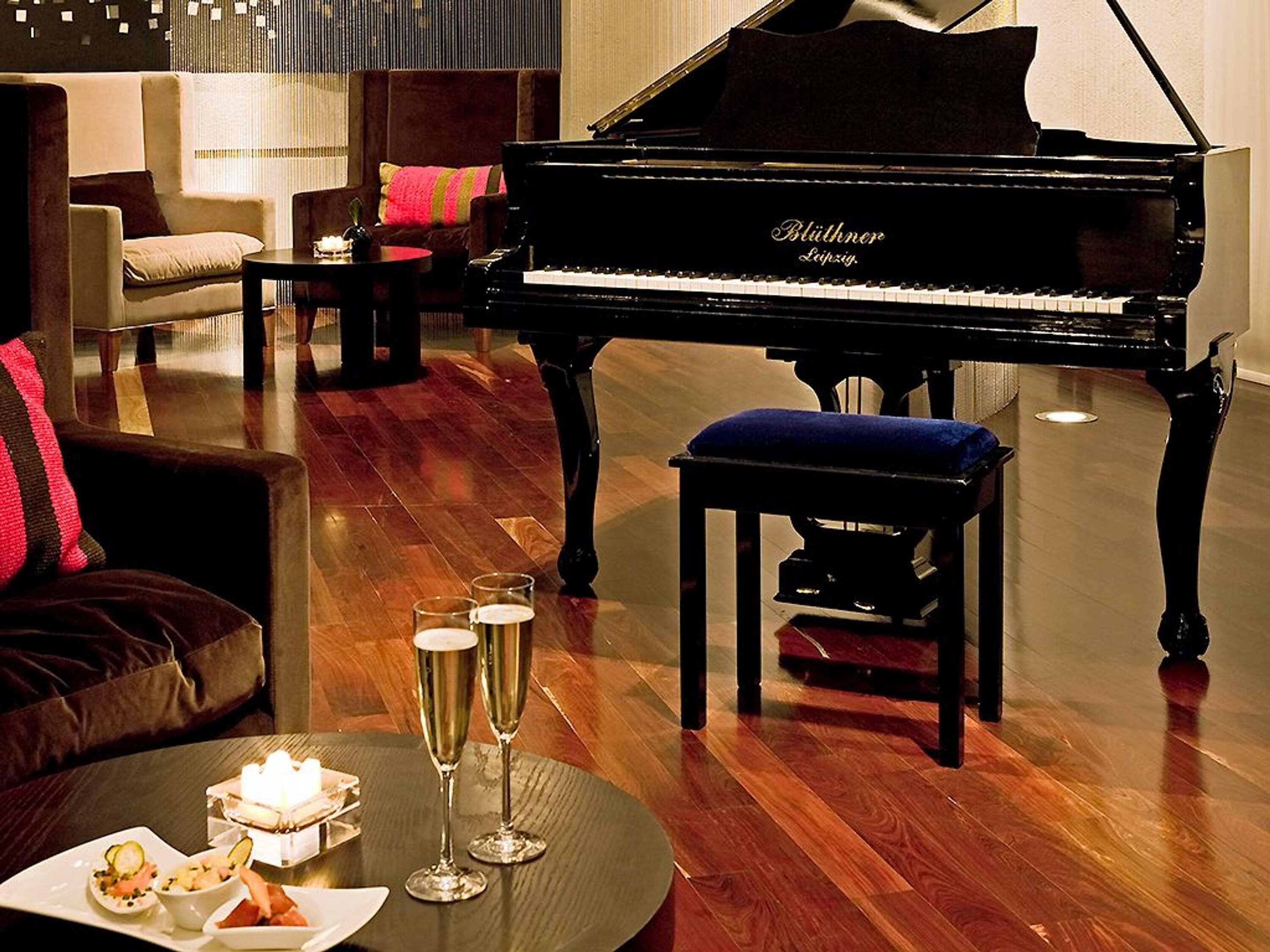 Un piano de cola, un taburete pequeño, una mesa con bebidas y un sofá en una habitación con piso de madera.