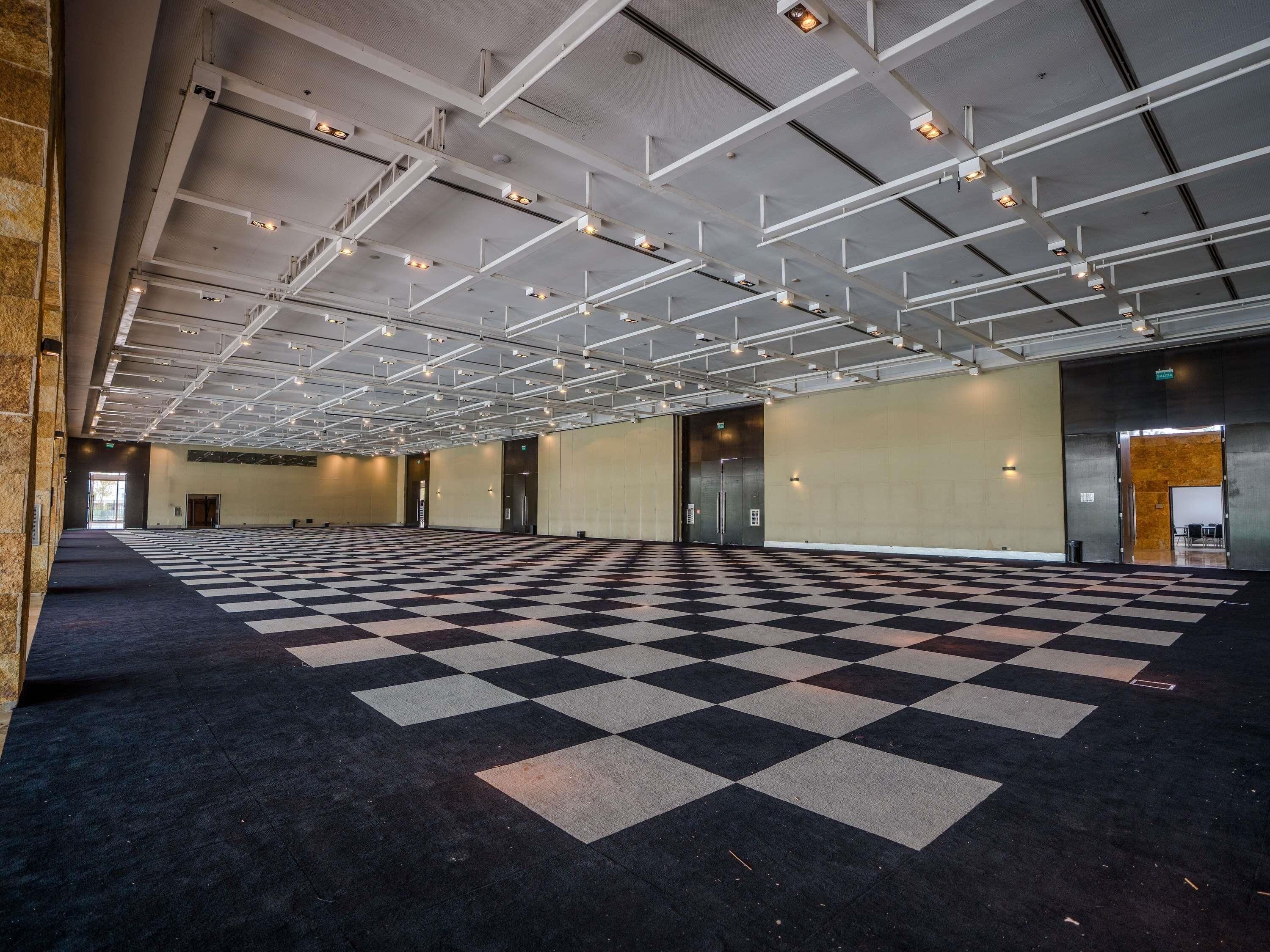 A spacious indoor area with a checkered floor, multiple doors, and a high ceiling with exposed beams and lighting fixtures.