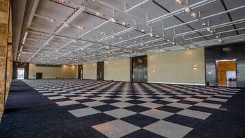 A spacious indoor area with a checkered floor, multiple doors, and a high ceiling with exposed beams and lighting fixtures.