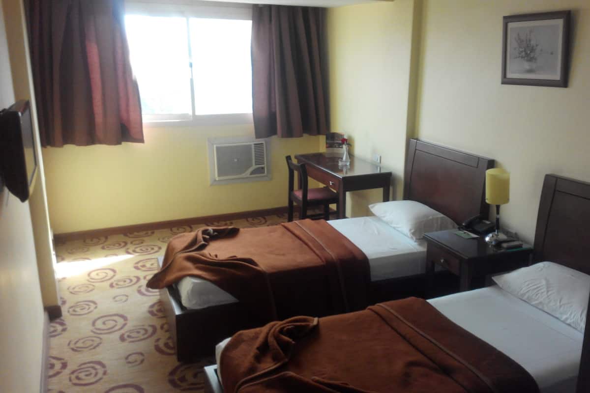 A hotel room with two beds, a desk, a chair, a lamp, and a picture on the wall.