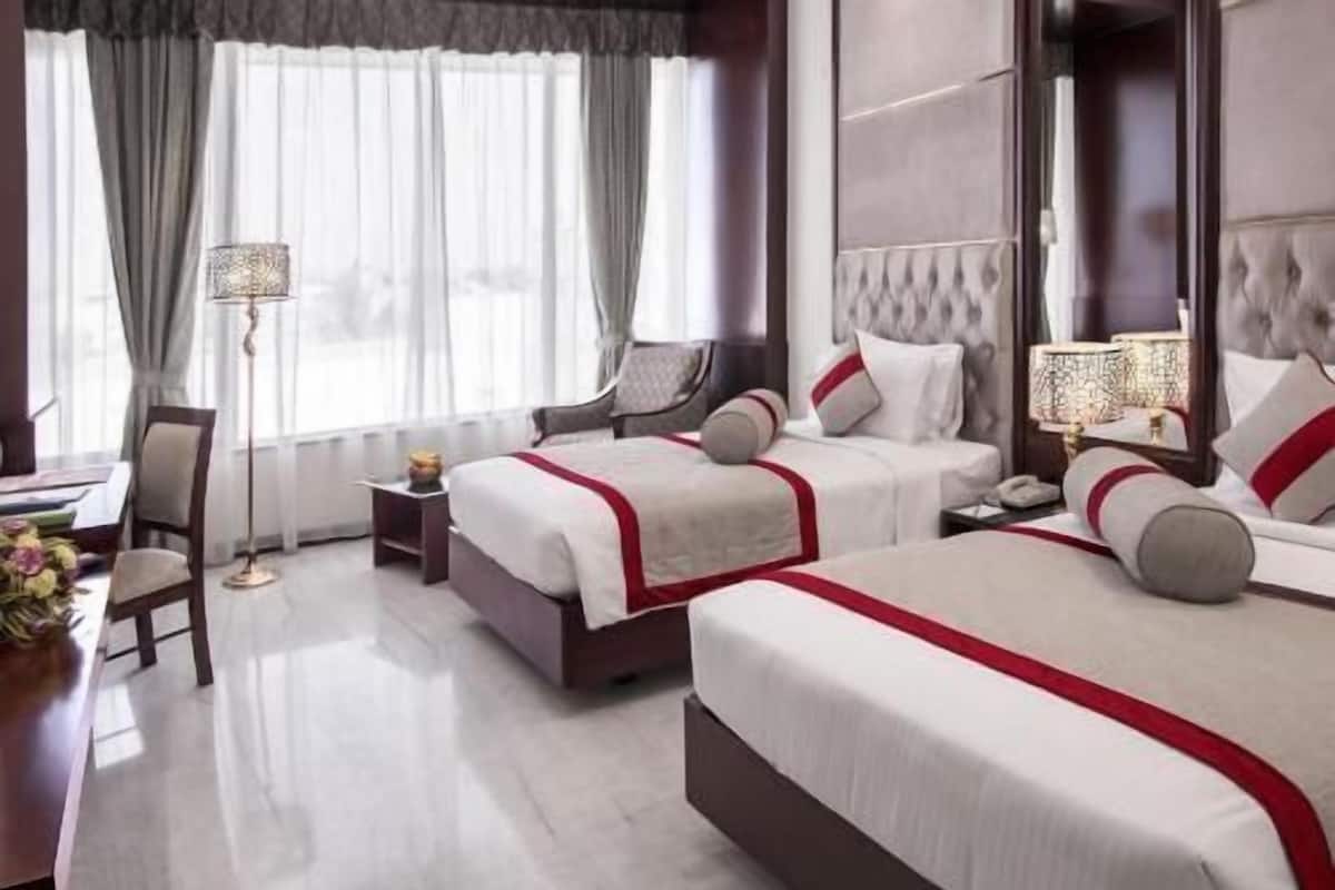A hotel room with two beds, a desk, a chair, and a bedside table.
