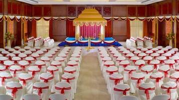 Un salón de conferencias con filas de sillas blancas adornadas con cintas rojas, un escenario con un telón de fondo azul y rojo, y un dosel dorado.