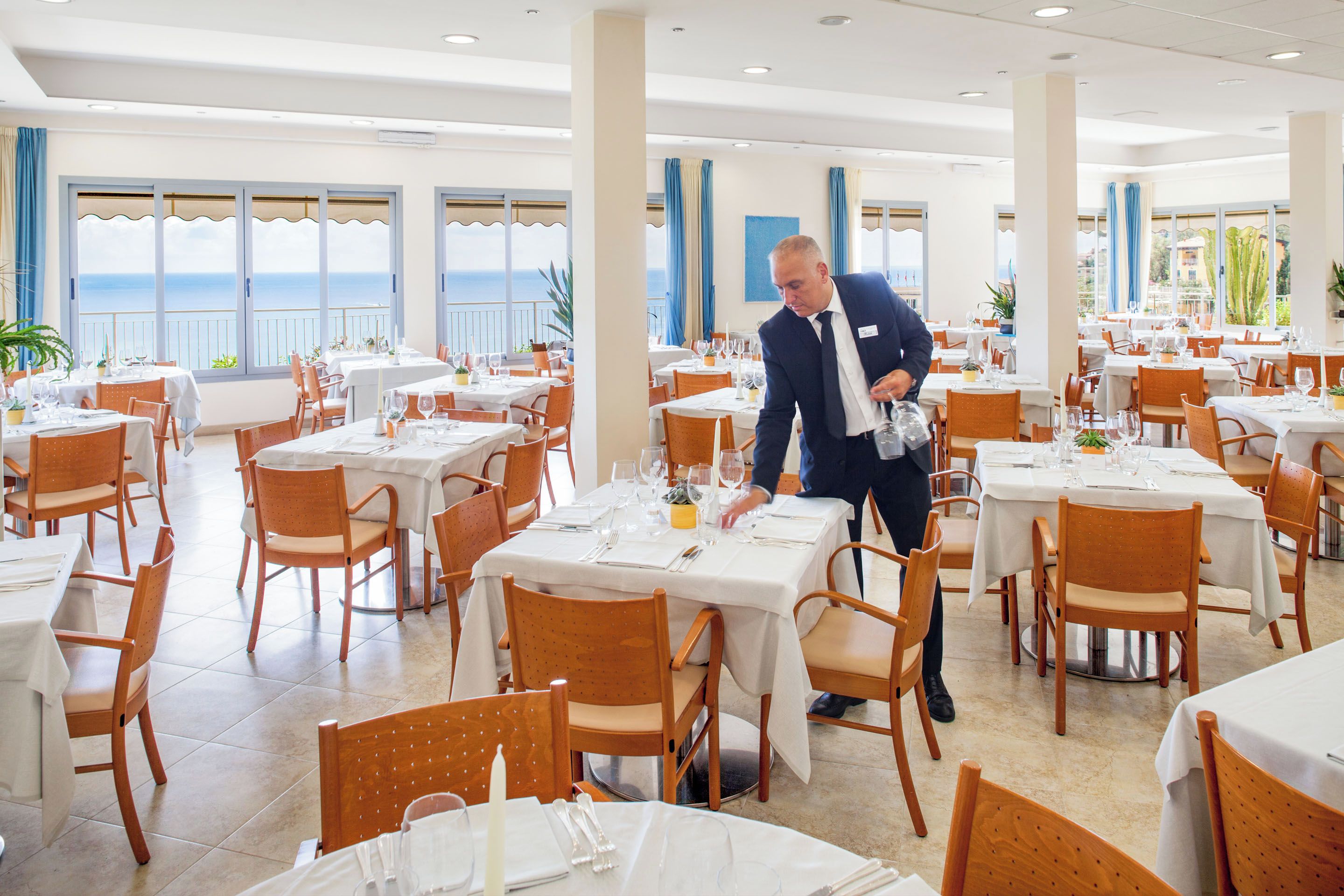 A restaurant with multiple tables, each set with white tablecloths, chairs, and dining utensils.