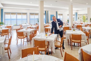 A restaurant with multiple tables, each set with white tablecloths, chairs, and dining utensils. - Hotel Metropol (Diano Marina)