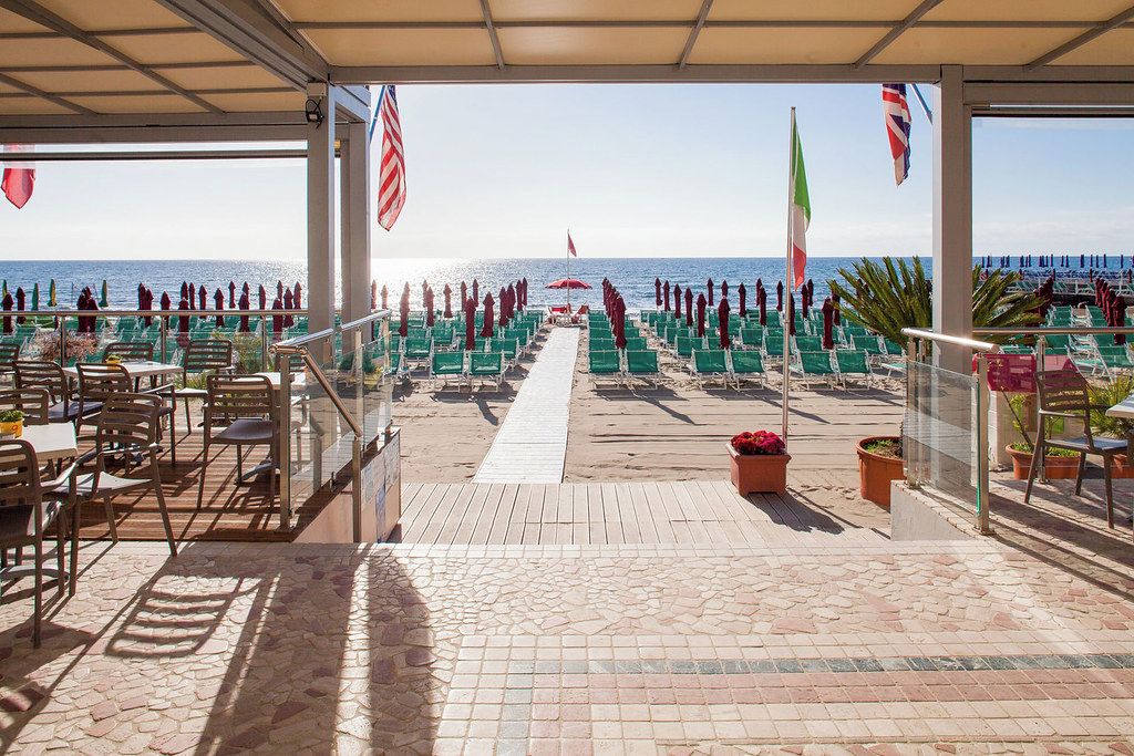 Un espace extérieur aménagé avec des sièges et offrant une vue sur la mer, comprenant un sol carrelé, des chaises, des tables et des plantes en pot.