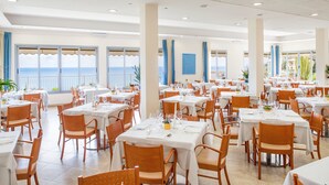 Un comedor amplio con varias mesas y sillas, ventanas grandes con vista al mar y un diseño de interiores moderno.