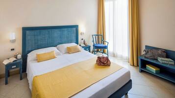 A hotel room with a large bed, a bedside table with a lamp, a chair, and a bench with a bag and box.