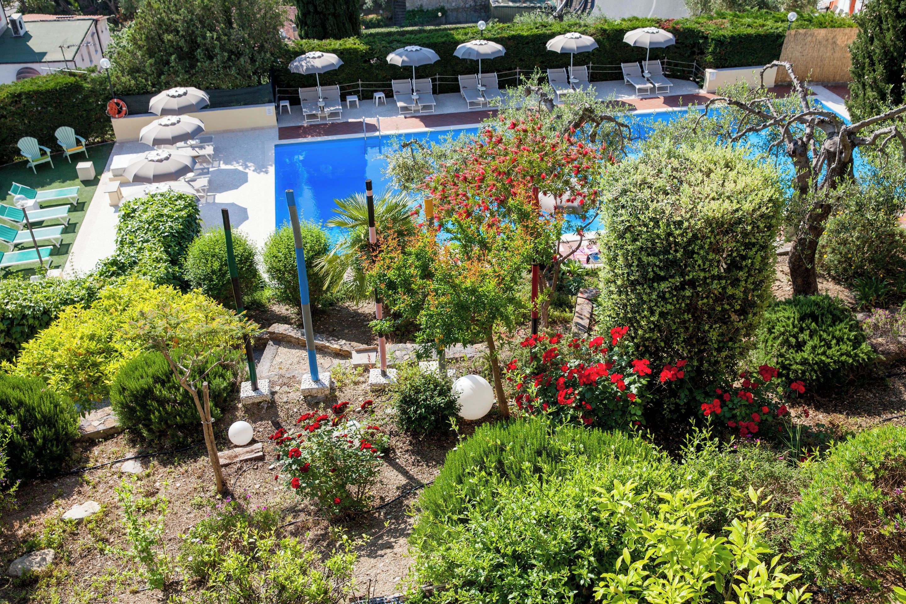 Un espace piscine agrémenté de chaises longues et de parasols, entouré de jardins et d’arbres bien entretenus.