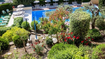 A pool area with lounge chairs and umbrellas, surrounded by well-maintained gardens and trees.