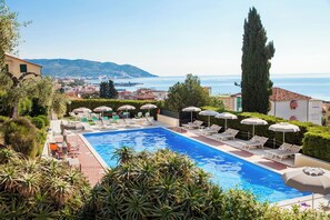Una piscina con tumbonas y sombrillas, rodeada de vegetación y con vistas a una ciudad costera.