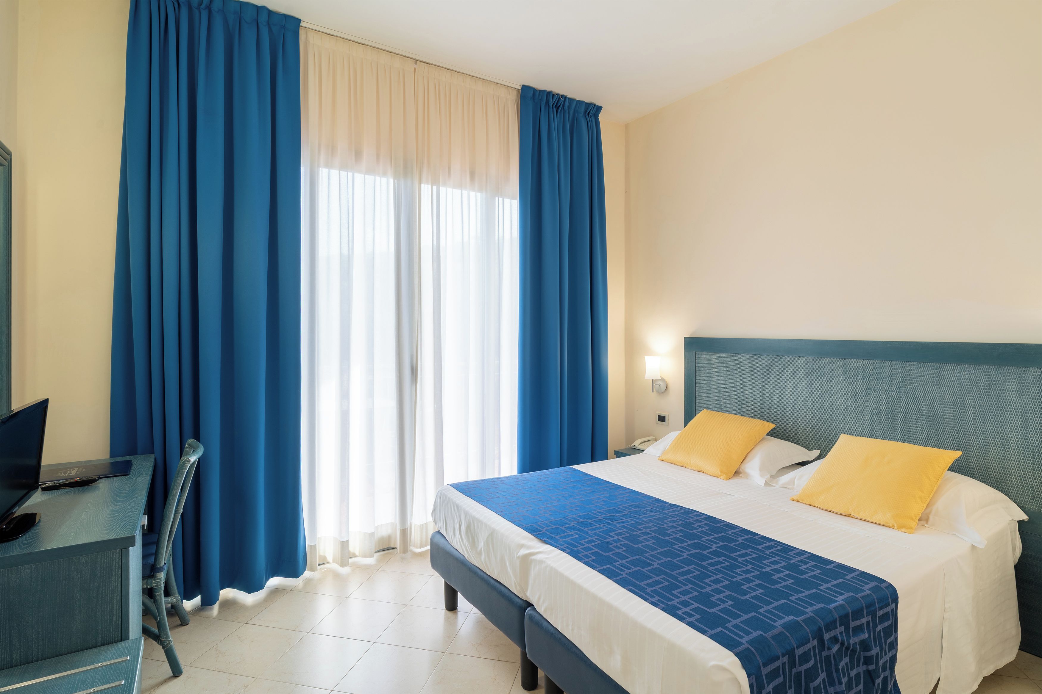 Een hotelkamer met een bed, een bureau en gordijnen.