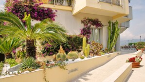Un edificio con balcón, un jardín de cactus y flores, y un camino empedrado.