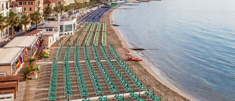 A beach with rows of green umbrellas and lounge chairs, a sandy shore, and buildings in the background.