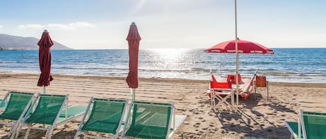 Una playa con sillas de descanso verdes y sombrillas rojas.