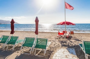 Una playa con sillas de descanso verdes y sombrillas rojas.