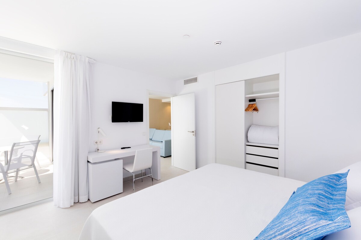 A modern hotel room with a bed, a desk, a chair, a TV, and a wardrobe.