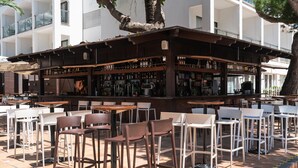 Un espace bar extérieur doté de différents types de sièges, notamment des tables et des chaises, ainsi que d’une variété de bouteilles et de verres disposés sur des étagères.