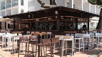An outdoor bar area with multiple seating options, including tables and chairs, and a variety of bottles and glasses on shelves.