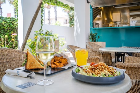 A dining table with a plate of salad, a glass of white wine, a glass of orange juice, and a basket of fries.
