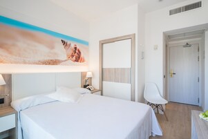 Ein Hotelzimmer mit Bett, Schreibtisch, Stuhl, einem Gemälde und einer Tür.