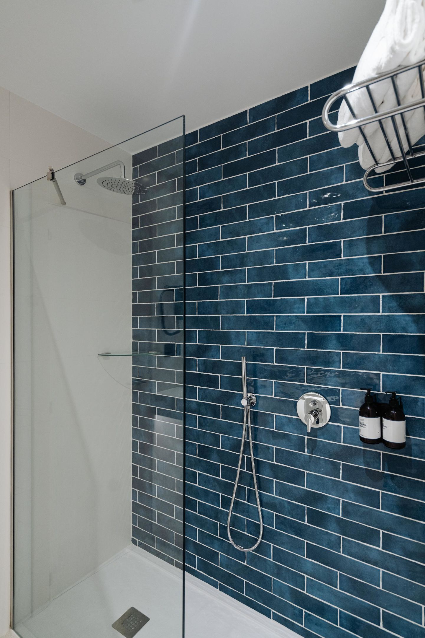 Een moderne badkamer met een douchecabine van glas, een wand betegeld met blauwe tegels en een handdoekrek.