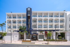 Ein mehrstöckiges Hotel mit einem zentralen Eingang, Balkonen und wolkenlosem, blauem Himmel.