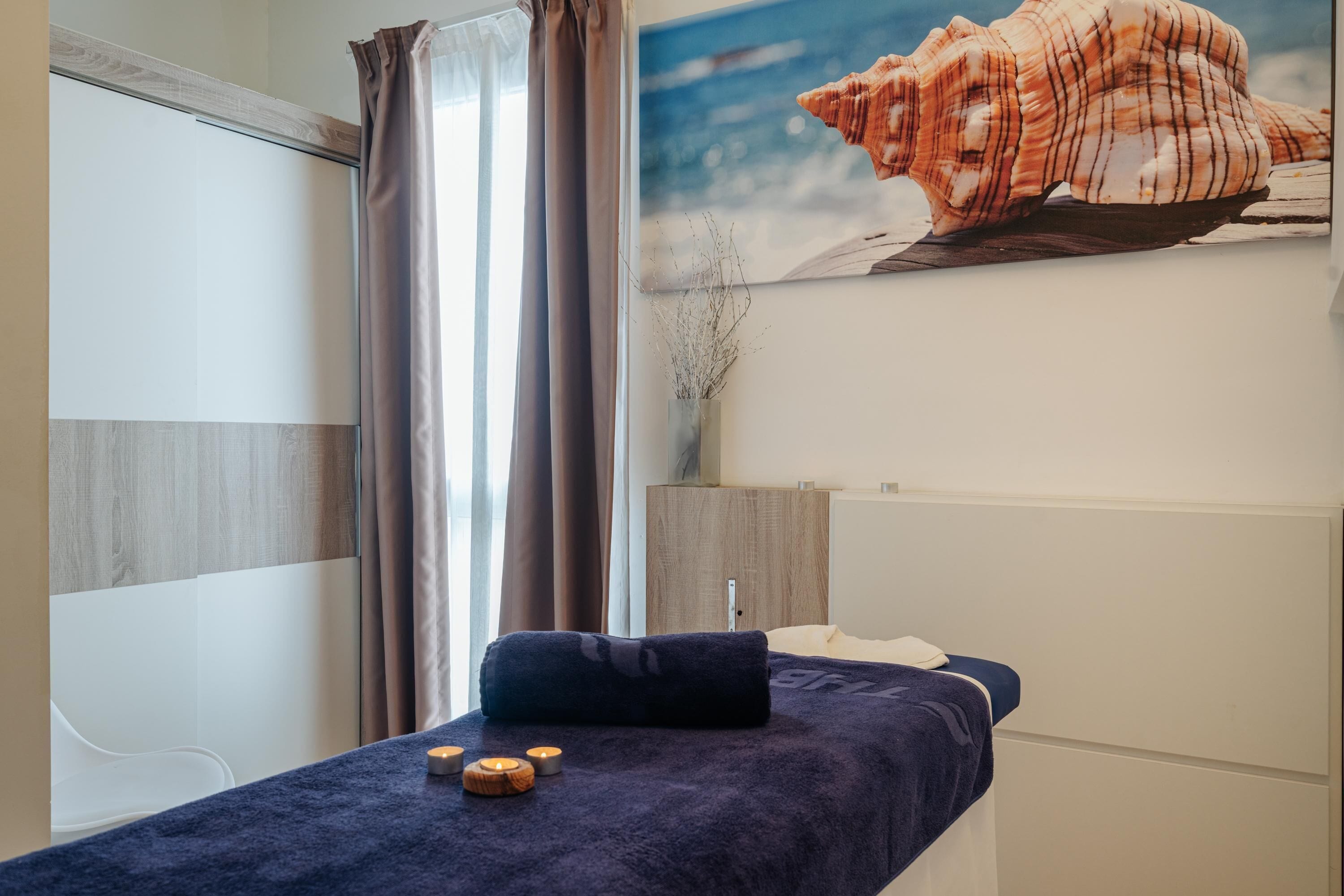 Un cuarto de spa con una camilla de masaje, velas y una gran concha decorativa en la pared.