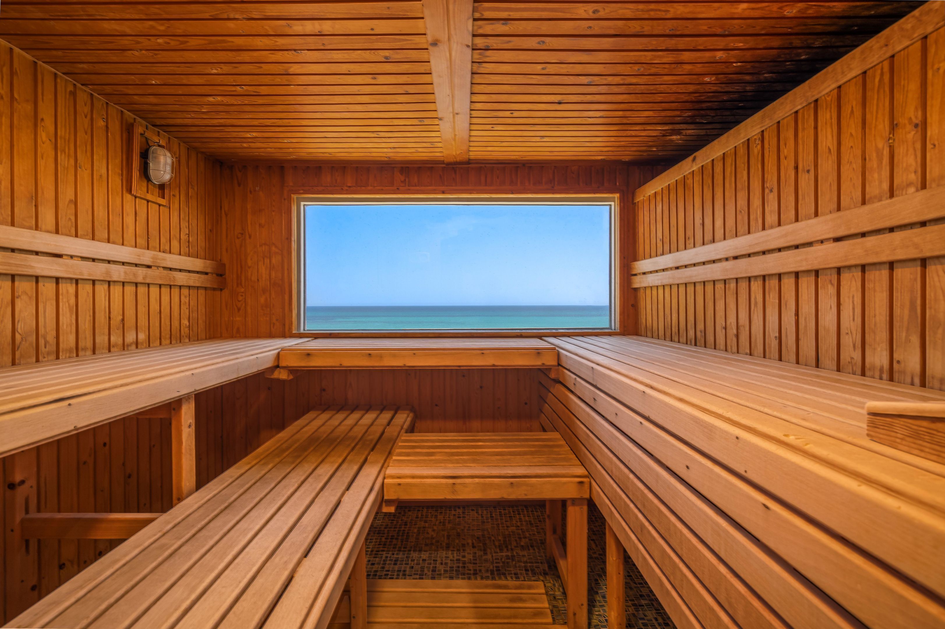Un sauna en bois, doté de bancs et d’une fenêtre donnant sur la mer.