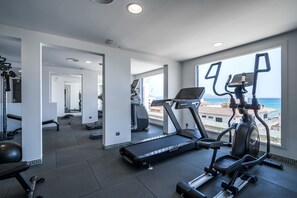 Een moderne sportschool met loopbanden en elliptische trainers, grote ramen met uitzicht op zee, en een ruime indeling.