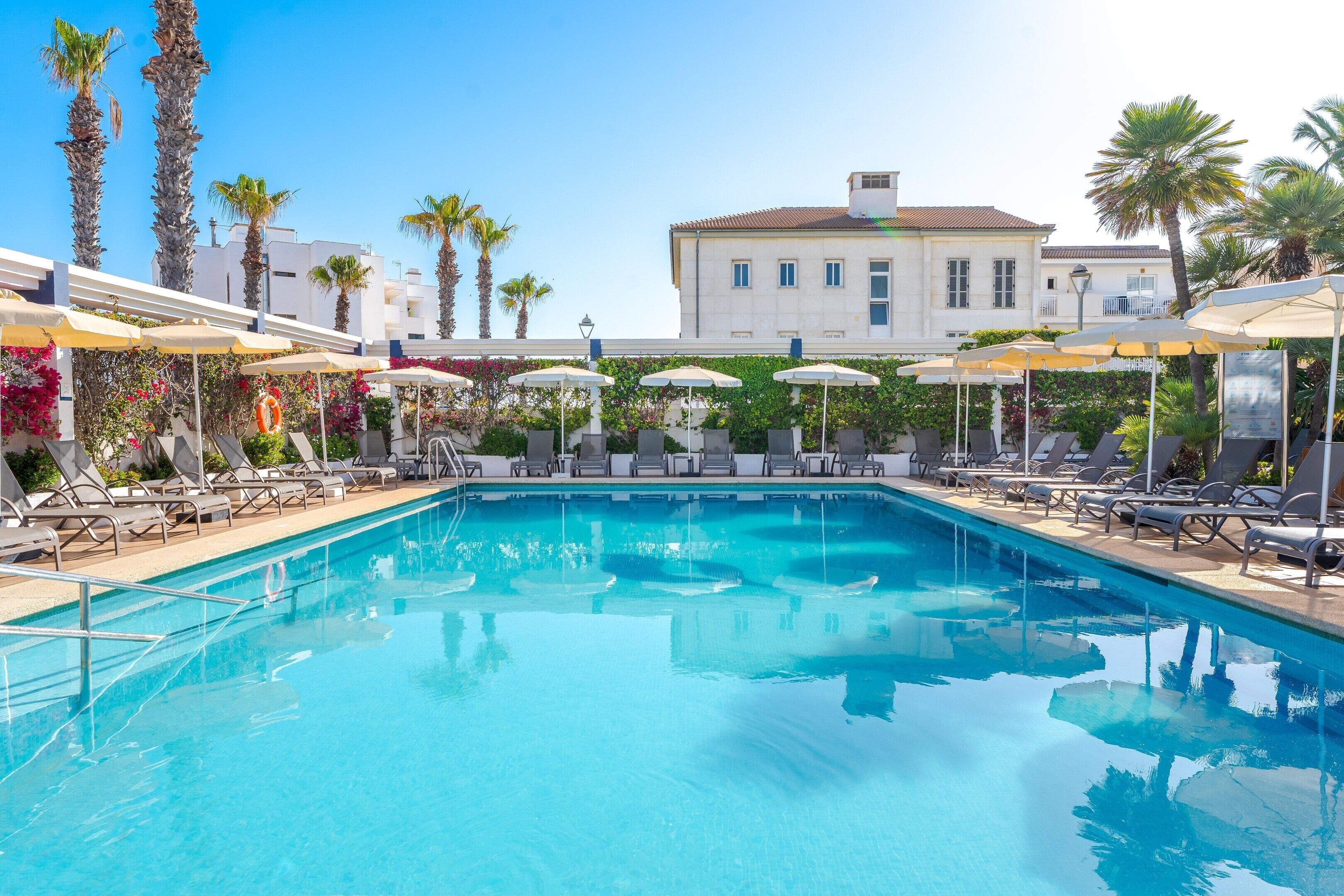 Una piscina al aire libre, sombrillas, sillones reclinables de piscina