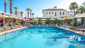 Una piscina al aire libre, sombrillas, sillones reclinables de piscina