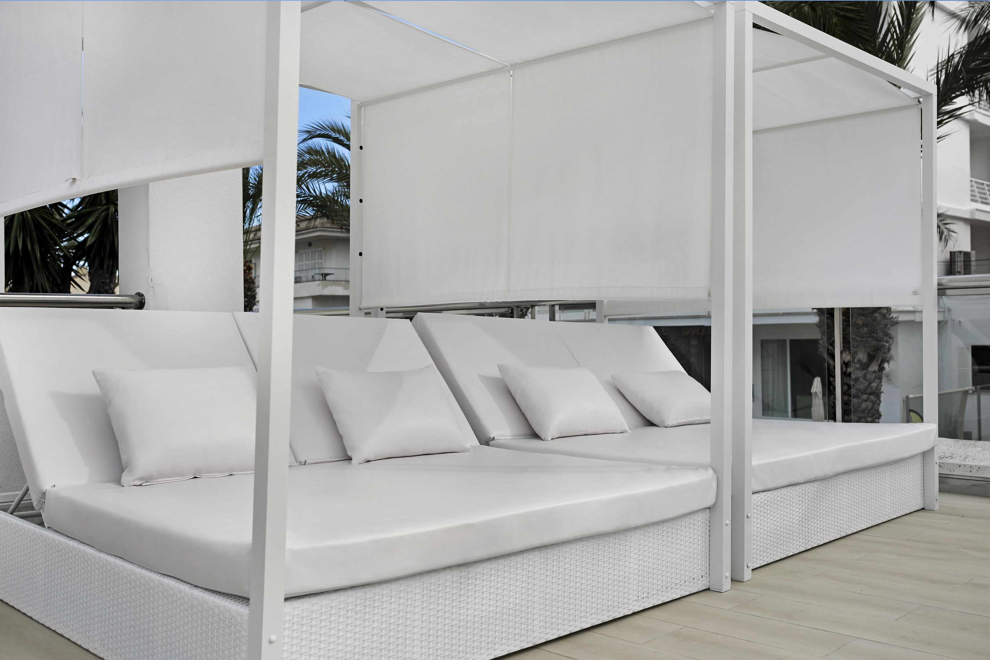 A white outdoor sofa with cushions, a covered area, and a view of a building with balconies.