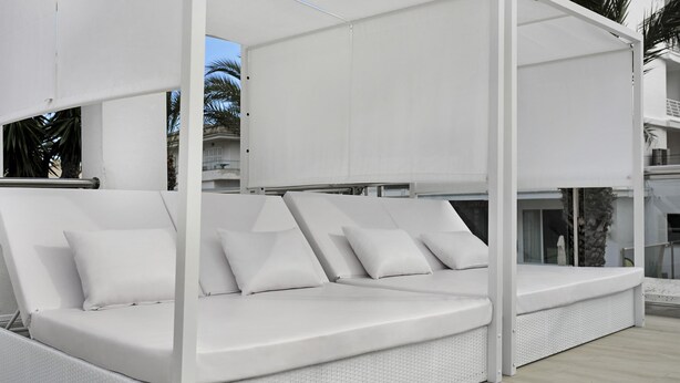 Un canapé d’extérieur blanc, doté de coussins, situé dans un espace abrité, avec vue sur un immeuble à balcons.