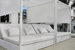 Un canapé d’extérieur blanc, doté de coussins, situé dans un espace abrité, avec vue sur un immeuble à balcons.
