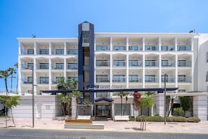 Un hôtel à plusieurs étages, doté d’une entrée centrale, de balcons et surplombant un ciel d’un bleu éclatant.