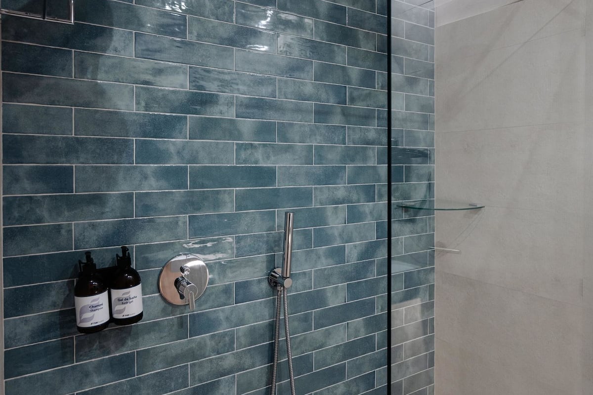Un espace douche moderne avec une porte en verre, des murs recouverts de carreaux bleus et un porte-serviettes en métal.