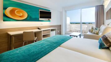 Habitación de hotel con cama, escritorio, silla, televisor y balcón con vista al mar.