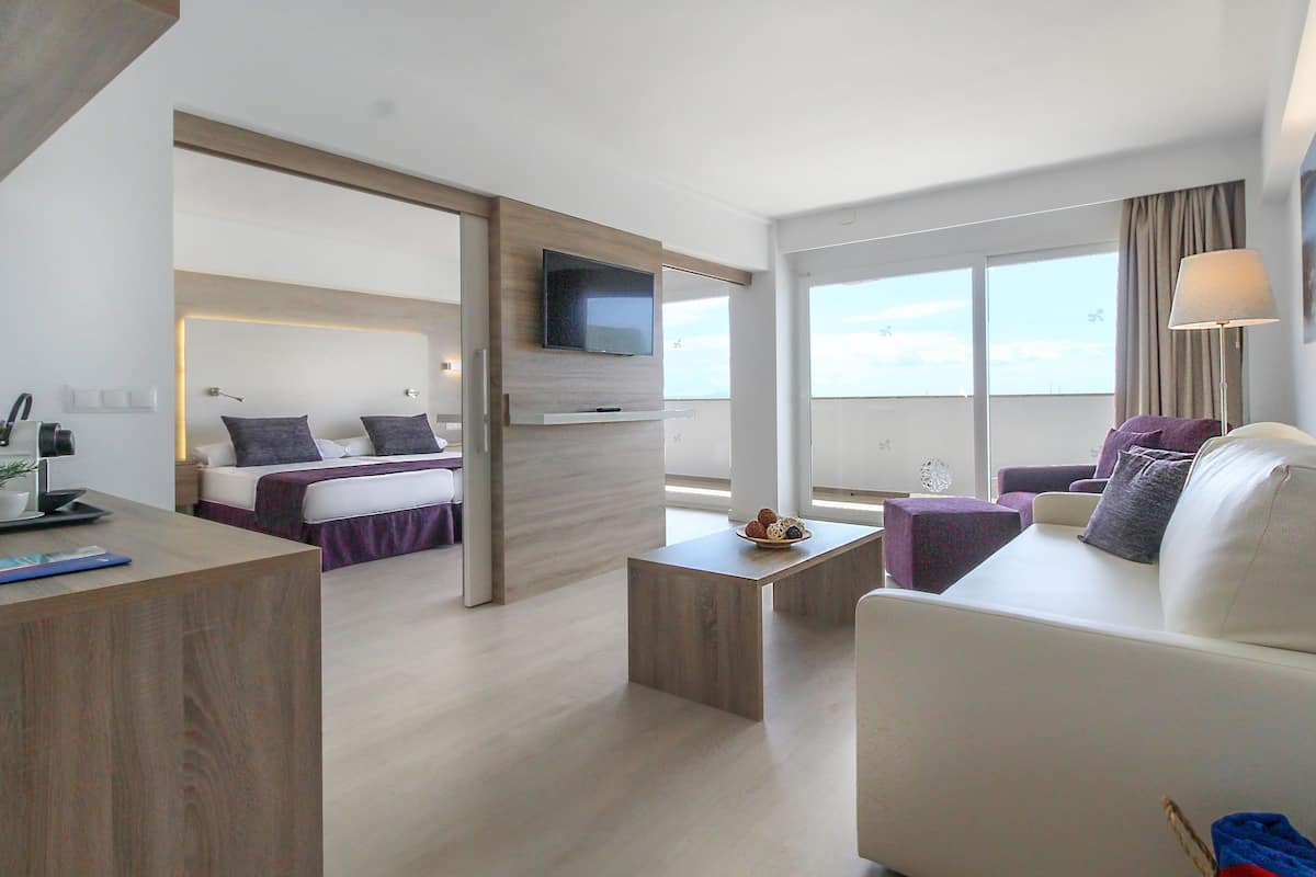 Una habitación de hotel moderna con cama, sofá, mesa de centro y televisión instalada en la pared.