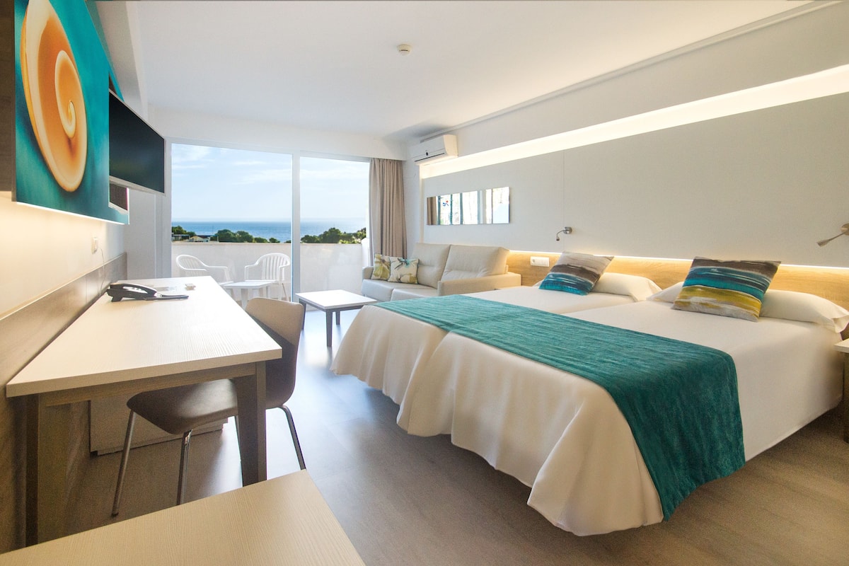 Una habitación de hotel moderna con una cama grande, un escritorio y vista al océano.