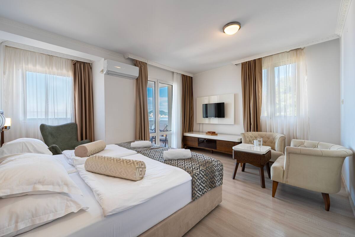 Une chambre d’hôtel avec un grand lit, deux fauteuils, un bureau et une télévision.