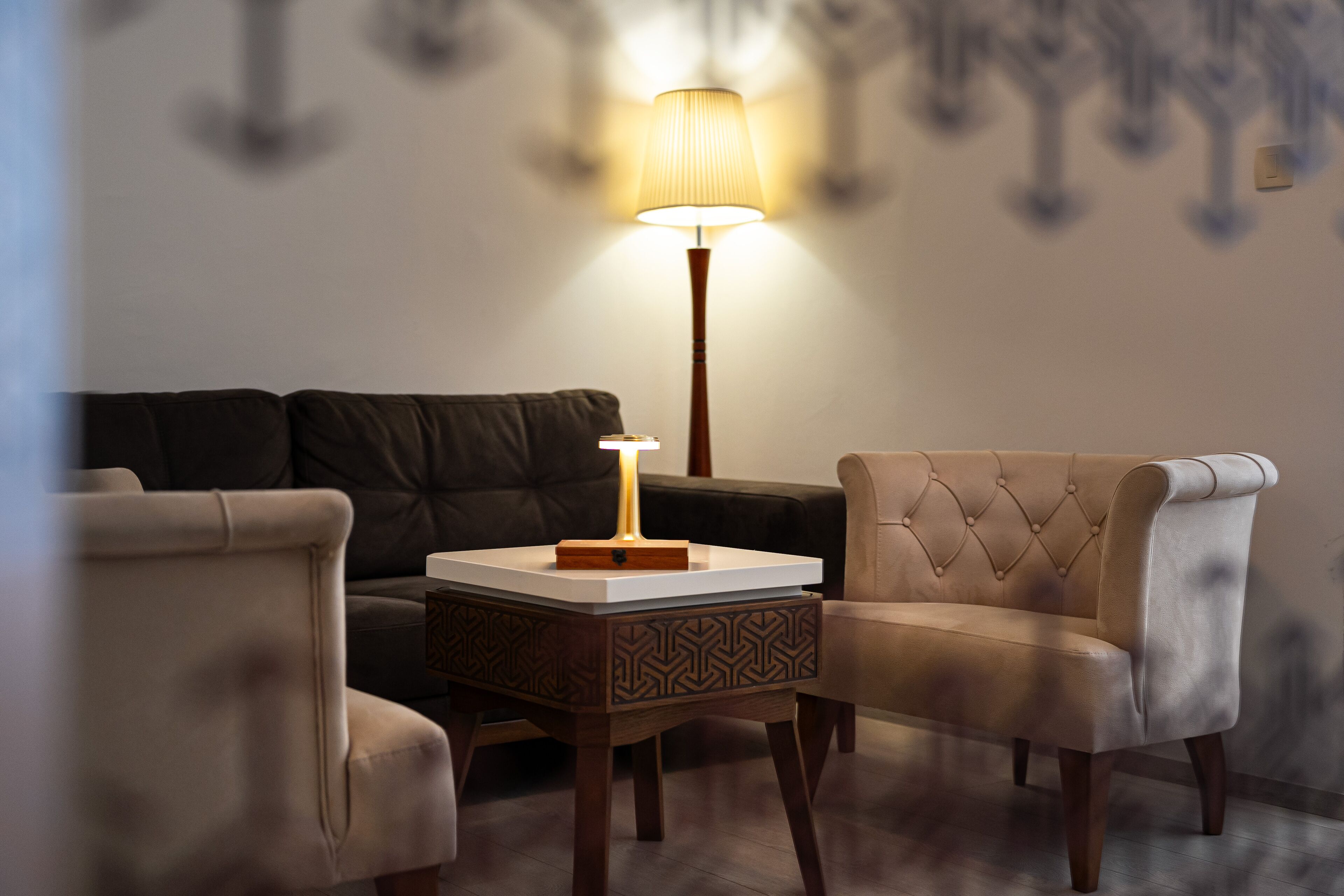 Una sala de estar con un sofá, dos sillones, una mesita de noche con una lámpara y una mesita lateral con diseño.