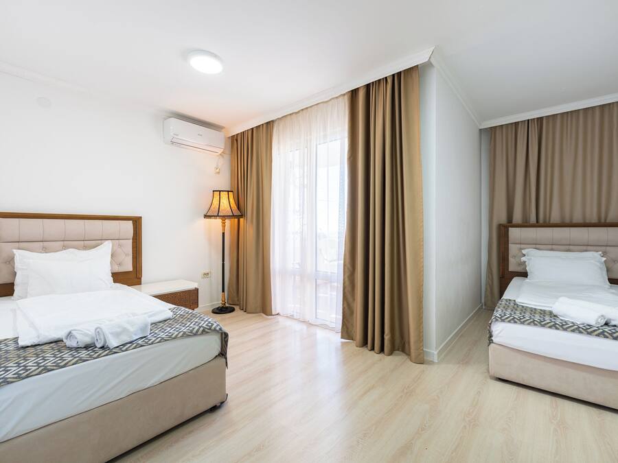 A hotel room with two beds, a bedside table, a lamp, and a window with curtains.