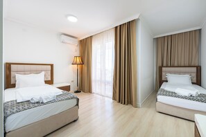 Ein Hotelzimmer mit zwei Betten, einem Nachttisch, einer Lampe und einem Fenster mit Vorhängen.