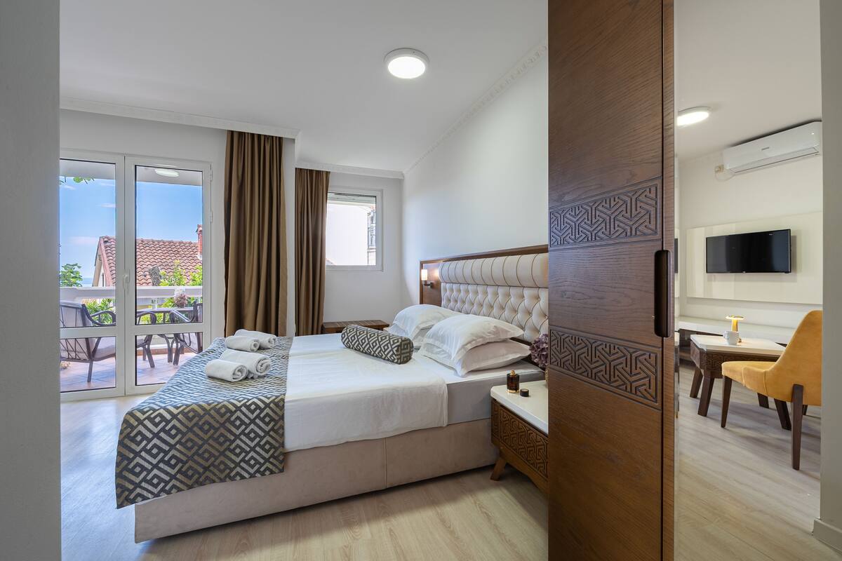 Une chambre d’hôtel avec un grand lit, une télévision, un coin repas et un balcon offrant une vue sur les bâtiments.
