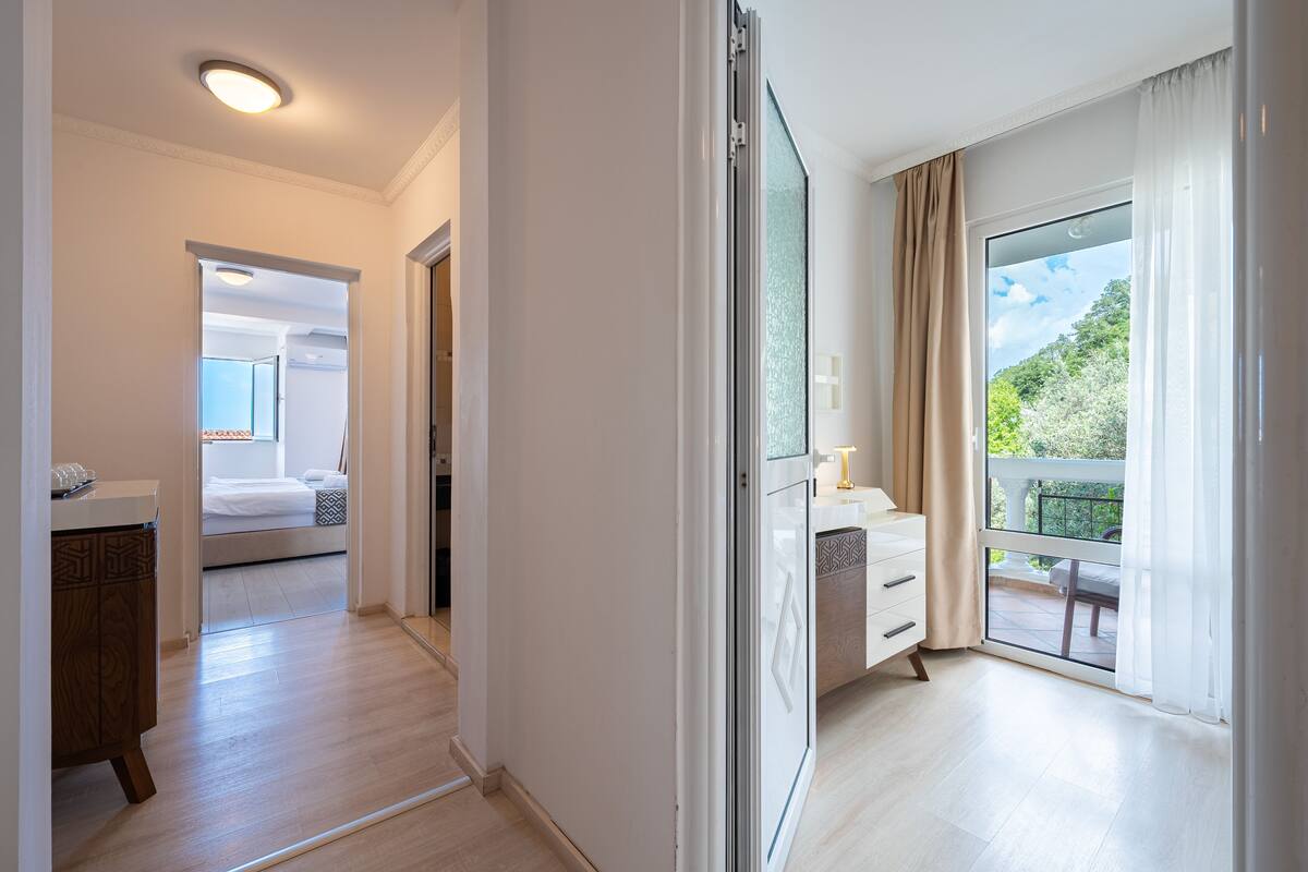 Une chambre d’hôtel moderne avec un balcon, un lit, une commode et une vue sur la verdure environnante.