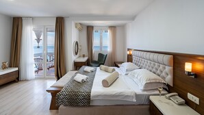 Habitación de hotel con una cama grande, una mesita de noche con lámpara, una silla y vista al mar a través de una puerta corrediza.