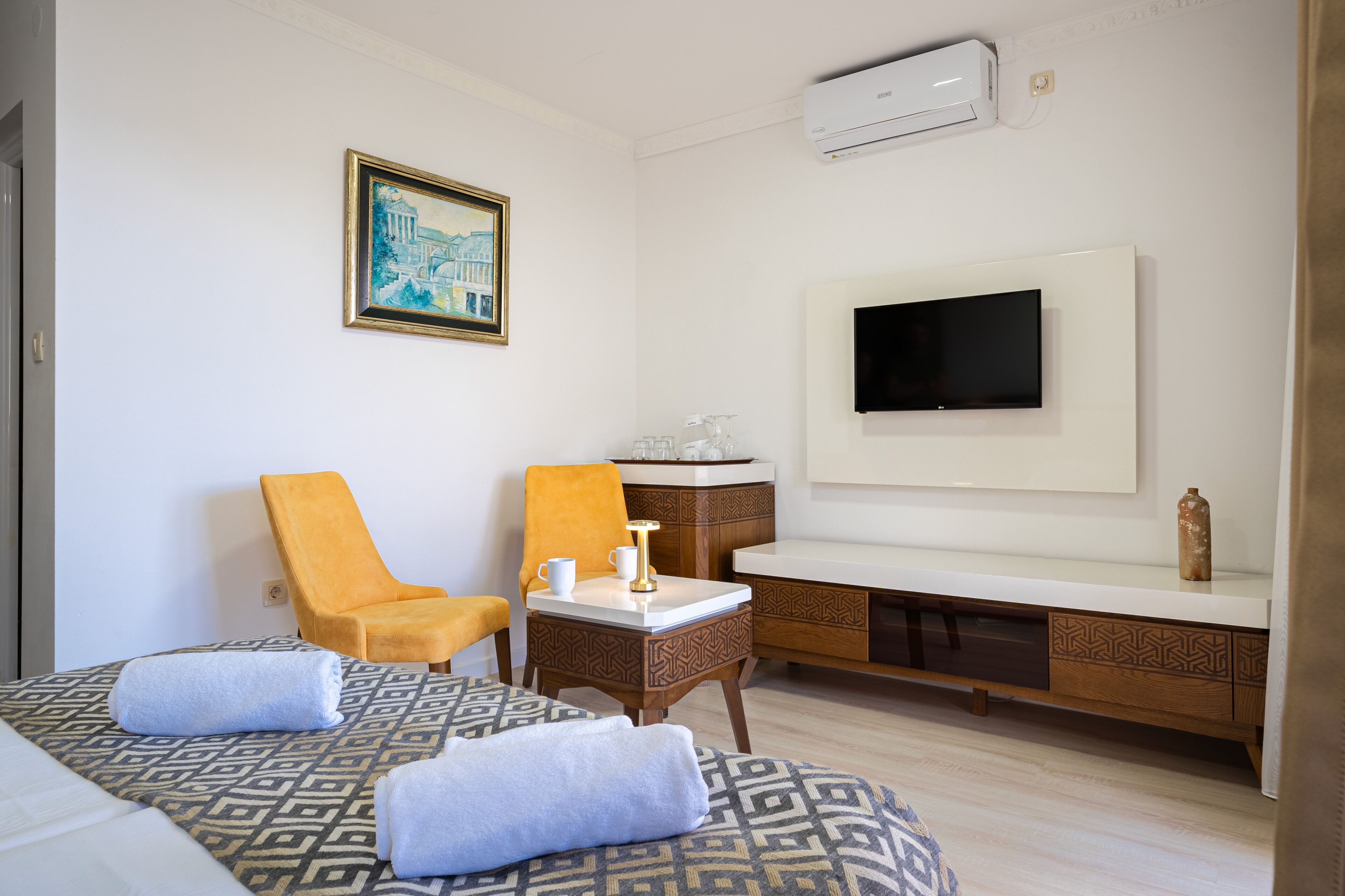A hotel room with two beds, a TV, a painting, and a minibar.