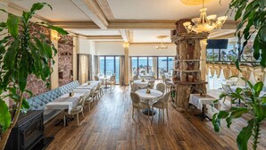 Un restaurante con suelo de madera, mesas y sillas blancas, una pared de piedra y vistas al mar.