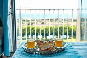 Bandeja de café da manhã com torradas, geleia e suco de laranja em uma varanda com vista para áreas verdes e edifícios.
